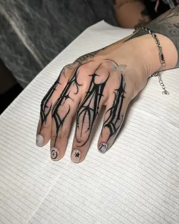 Mão apoiada no papel com letras góticas pretas tatuadas nos quatro dedos