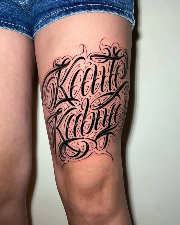 Coxa com dois nomes em lettering chicano preto, cheio de floreios, logo acima do joelho