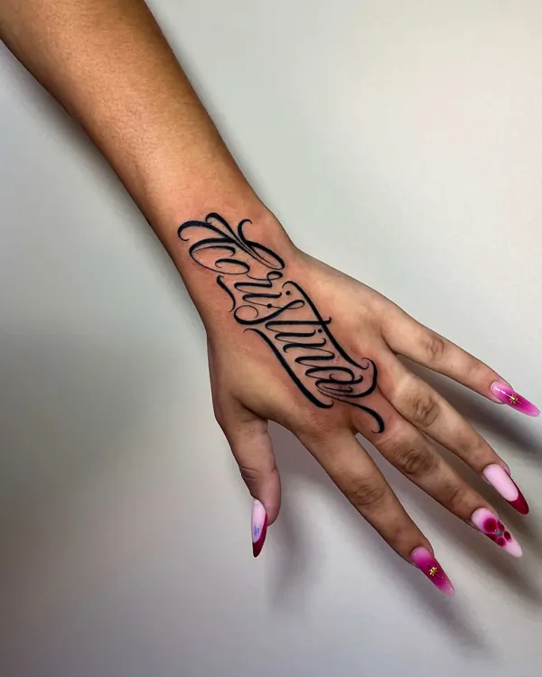 Mão feminina com um nome em script fino na lateral, do punho até o dedo