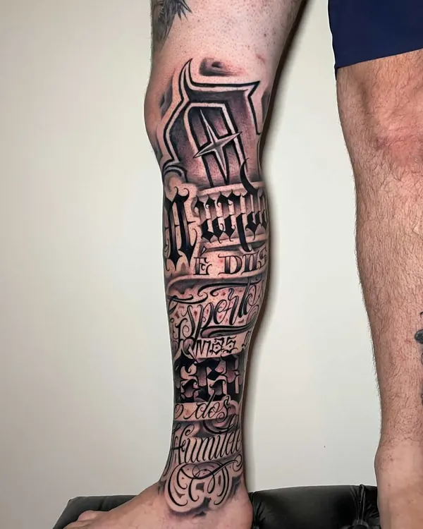 Perna com a canela fechada por frases em lettering chicano preto e cinza, do joelho ao tornozelo