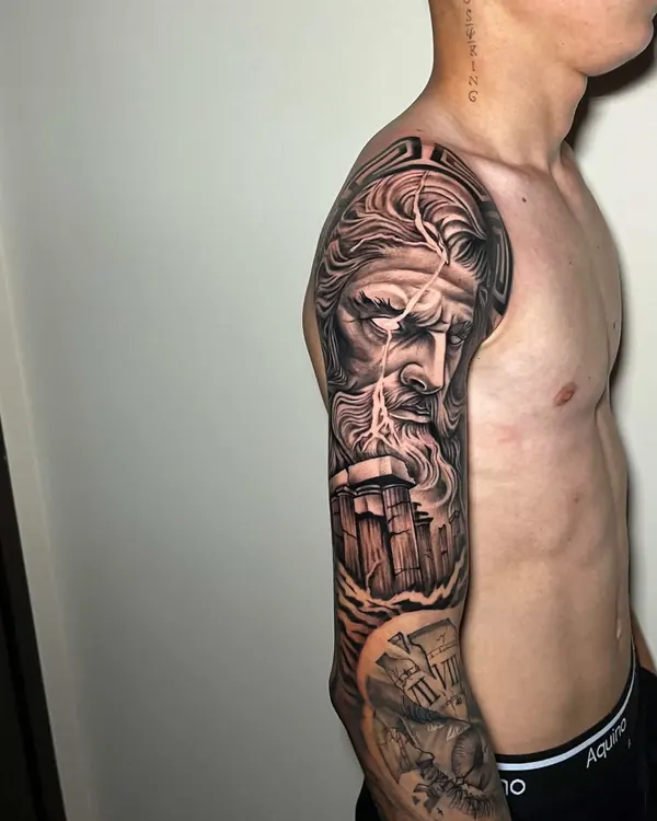 Braço fechado em black and grey realista com o rosto de Zeus, raios e colunas de templo